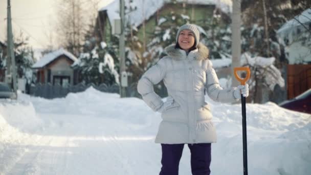 Gelukkig jonge vrouw die zich voordeed op camera met schop in voorsteden in de winter. — Stockvideo