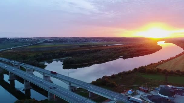 Traffico di auto sul ponte autostradale al tramonto. Vista aerea. Bellissimo paesaggio, cielo, foresta, campo e fiume . — Video Stock