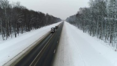 Kışın uçan araba ve kamyonlar. Yol karla ve ağaçlarla çevrili.