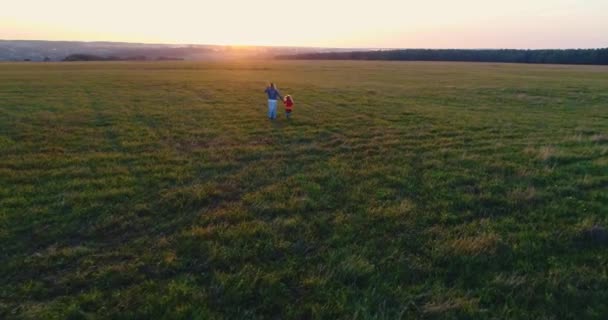 Kızıyla birlikte gün batımında tarlada yürüyen ve kaçan genç bir anne. — Stok video