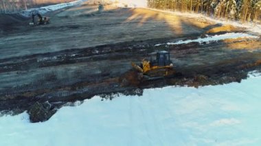 İki buldozer kumları aşıyor, kışın yol yapıyor. Ormanların tahrip edilmesi, inşaat