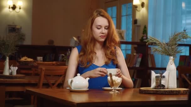 La belle fille aux cheveux roux assise dans un café, buvant du thé et souriant — Video