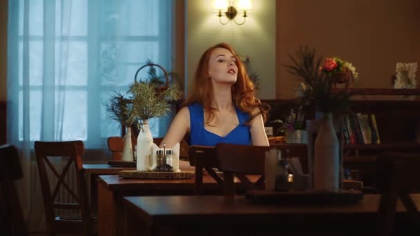 Het mooie sexy meisje met rood haar zit in cafe, poseren en glimlachen — Stockvideo