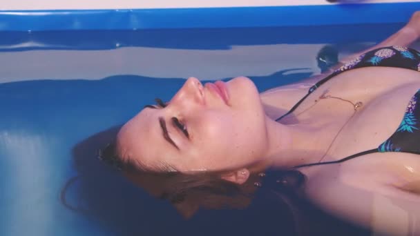 Krásná dívka v bikinách relax těšit zavírá oči v modré vodě Lázeňský bazén koupel. — Stock video