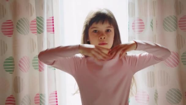 Vicces kifejező aranyos művészi kislány hosszú haj pózok, tánc ablak mellett — Stock videók
