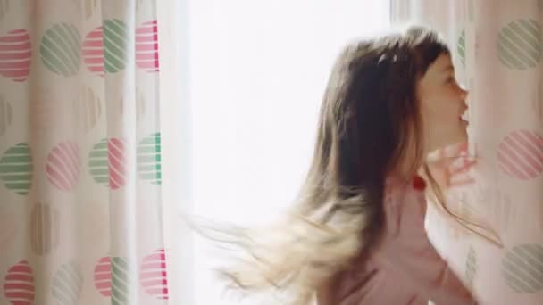 Vicces aranyos művészi kifejező kislány hosszú haj énekelni és táncolni ablak közelében — Stock videók