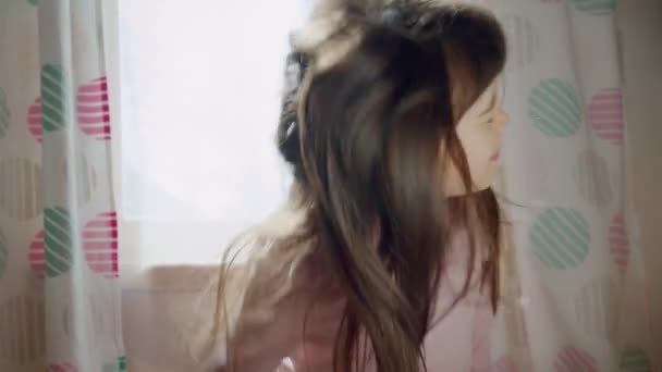 Komik, sevimli, sanatsal küçük kız uzun saç pozları verir, pencerenin yanında dans eder. — Stok video