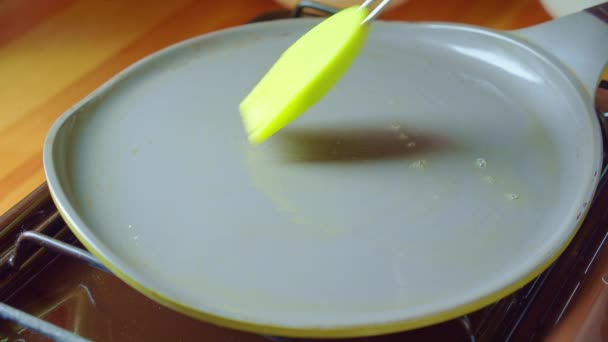 Mano con pennello in silicone verde spalma il burro su una padella calda sul fornello in cucina . — Video Stock