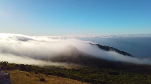 4k videó fehér felhőkről, amint átkelnek a hegycsúcsokon Madeira szigetén, Portugáliában. Napkelte van. Ez egy gyönyörű kilátás nyílik a repülő felhők, amelyek lefedik a tájat, és megy le — Stock videók