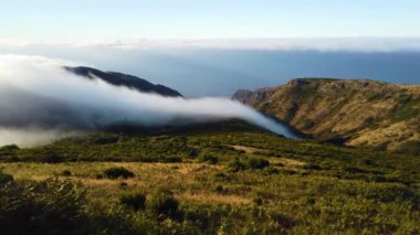 Portekiz 'deki Madeira adasındaki dağların üzerinden geçen beyaz bulutların 4k videosu. Güneş doğuyor. Uçan bulutların manzarası manzarayı kaplıyor ve batıyor.