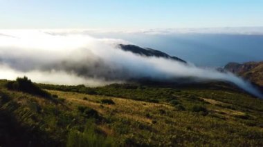 Portekiz 'deki Madeira adasındaki dağların üzerinden geçen beyaz bulutların 4k videosu. Güneş doğuyor. Uçan bulutların manzarası manzarayı kaplıyor ve batıyor.