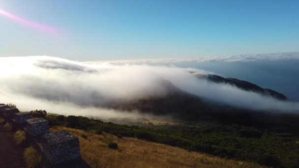 Vídeo em 4K de nuvens brancas a sobrevoar picos de montanha na ilha da Madeira, Portugal. Há um nascer do sol. É uma bela vista das nuvens voadoras que cobrem a paisagem e descem — Vídeo de Stock