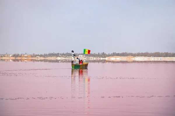 LAC RoSE, SENEGAL - KWIECIEŃ 22, 2019: Człowiek niesie turystów na drewnianej łodzi na różowym jeziorze w pobliżu miasta Dakar. To jest słone jezioro Retba. Miejscowi w jeziorze ręcznie wydobywają sól.., — Zdjęcie stockowe