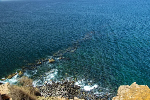 Sjöklippa med svarta stenar på Goree ön, nära Dakar, Senegal. Det finns det turkosa vattnet i Atlanten som är typiskt för Afrika. Det är en vacker solig dag.. — Stockfoto