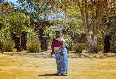 Goree, Senegal, 22 Nisan 2019: Birleşik Senegal kadınının kafasında bir meyve sepeti var ve tipik renkli geleneksel Senegl kıyafetleri giyiyor..