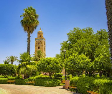 Fas'ın Marakeş'in Medine Mahallesi'ndeki Koutoubia Camii minaresi. Palmiyeli güzel yeşil bir bahçe vardır. Mavi gökyüzü arka planda.