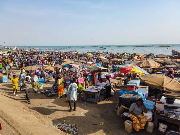 MBour, Senegal - 25 Nisan 2019: Dakar yakınlarındaki liman şehrindeki balık pazarında kimliği belirsiz Senegalli erkek ve kadınlar. Her yerde tezgahlar ve balıkçı tekneleri var..