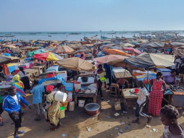 MBour, Senegal - 25 Nisan 2019: Dakar yakınlarındaki liman şehrindeki balık pazarında kimliği belirsiz Senegalli erkek ve kadınlar. Her yerde tezgahlar ve balıkçı tekneleri var..