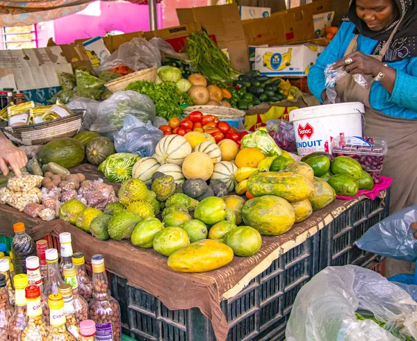 MBour, Senegal, AFRICA - April 22, 2019: Unidentified Senegalese woman sell fruits in her stall. Street fruit market where locals offers tropical fruits like melons, mangoes, oranges, lemons and — Stock Photo, Image