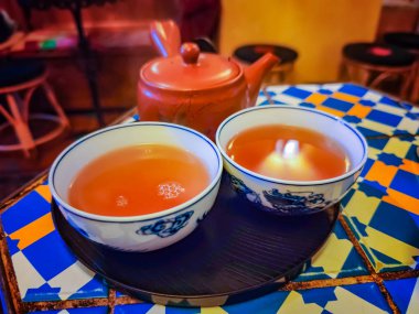 Renkli masada iki bardak kırmızı pu-erh çayı ve çaydanlık. Çay odasındaydı. Çay, toplantı ve sigara içmek için klasik Çin odası.