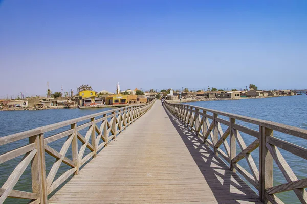 Jembatan kayu panjang yang mengarah ke laguna laut. Ini mengarah ke Pulau Fadiouth di Senegal, Afrika. Ini adalah latar belakang alam yang indah . — Stok Foto