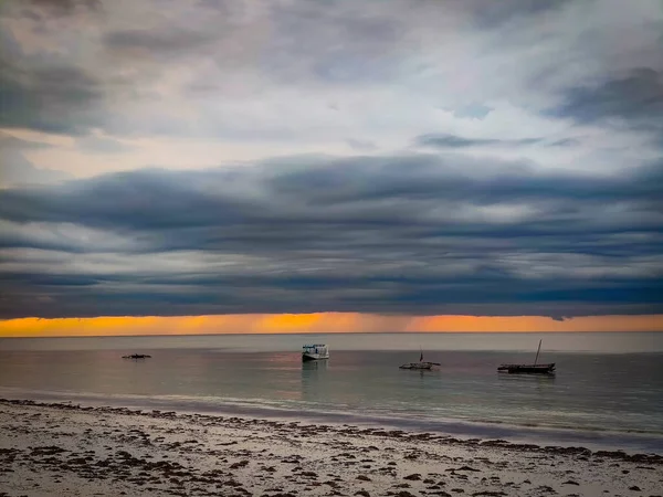 Hermoso amanecer en Kenia, África, playa Diani. Está lloviendo en la distancia y la tormenta se acerca. Hay pequeños barcos de madera en el agua . — Foto de Stock