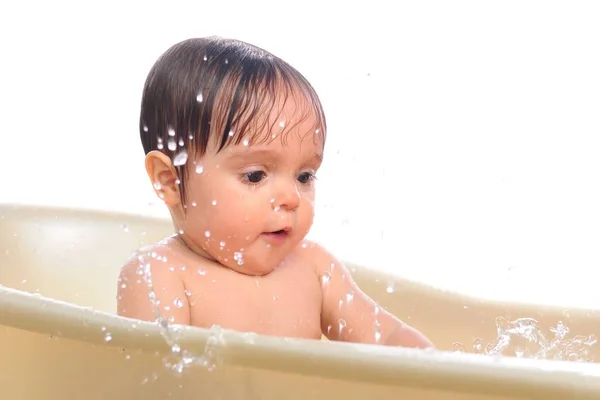 Menina senta-se no banho e espirra água — Fotografia de Stock