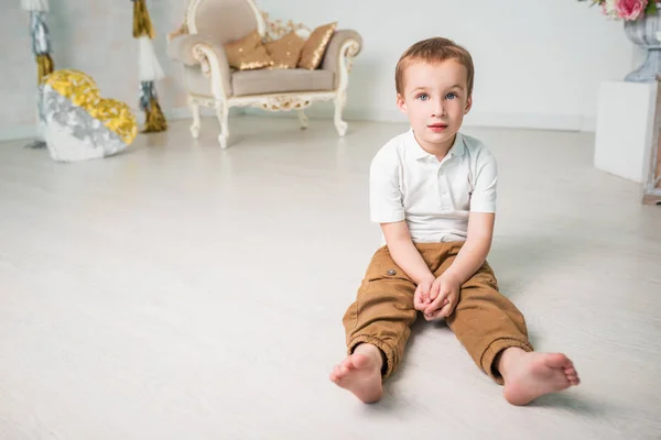 Обаятельный мальчик сидит на полу в уютной гостиной — стоковое фото