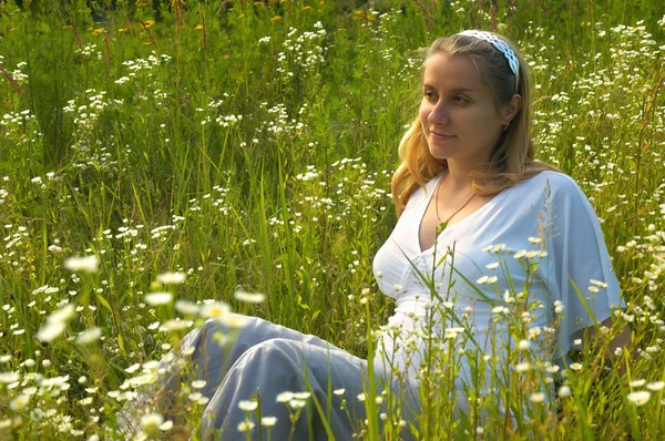 Mujer embarazada joven, sentada en un campo de flores, primavera — Foto de Stock