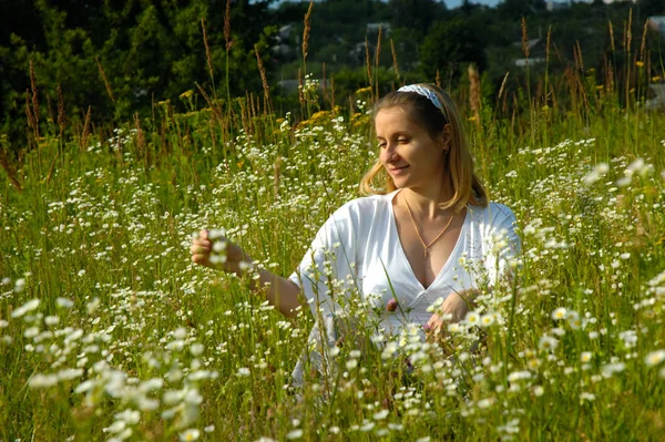 Mujer embarazada joven, sentada en un campo de flores, primavera — Foto de Stock