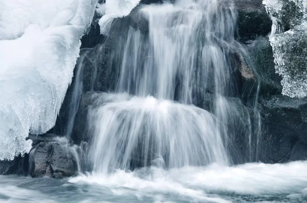 Schöner schneebedeckter Wasserfall, der in die Berge fließt — Stockfoto