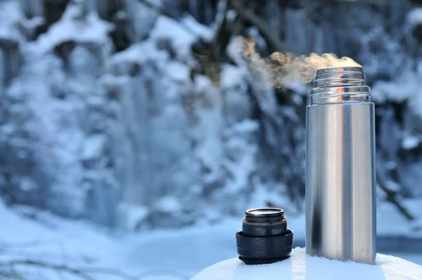 Thermoskan met een warme drank op de waterval van de berg — Stockfoto