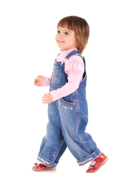 Mała dziewczynka w kombinezonie jeansowym spaceruje i uśmiecha się — Zdjęcie stockowe