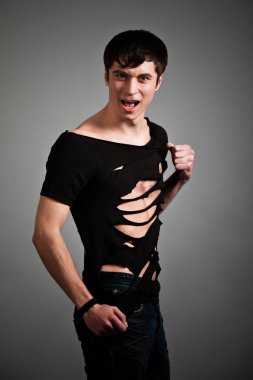 Siyah elbiseli öfkeli adam ayakta dikiliyor ve kameraya bakıyor.