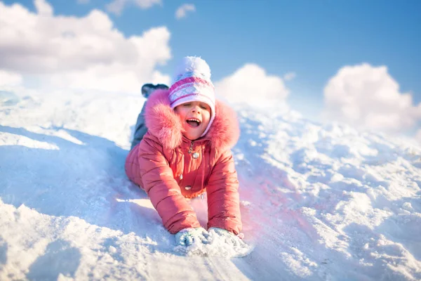 겨울 옷을 입은 어린 소녀 가손을 앞으로 내밀고 눈 위에서 내리막길을 걷고 있다 — 스톡 사진