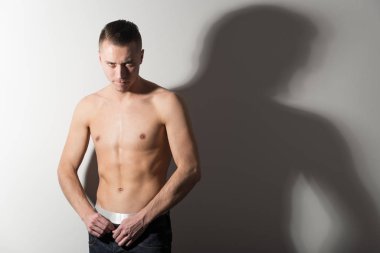 Kahverengi külotlu genç adam duruyor ve vücudunu gösteriyor.