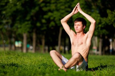 Yarı çıplak bir adam yeşil çimlerde oturuyor, meditasyon yapıyor ve yoga yapıyor.