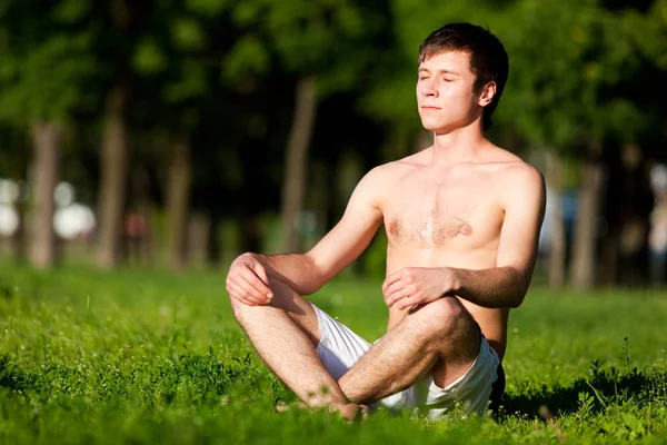 Yarı çıplak bir adam yeşil çimlerde oturuyor, meditasyon yapıyor ve yoga yapıyor.