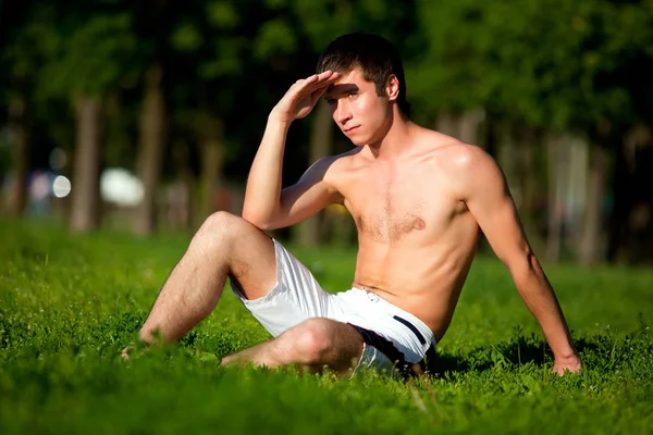 Half naked young man sitting on green grass and enjoying sunshine — Stock Photo, Image