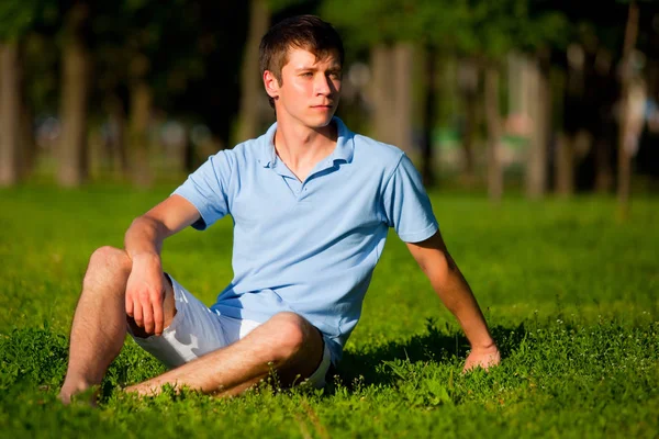 Giovane seduto su erba verde nel parco e guardando da parte — Foto Stock