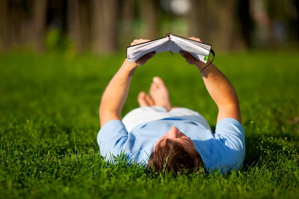 Giovane sdraiato su erba verde e libro di lettura — Foto Stock