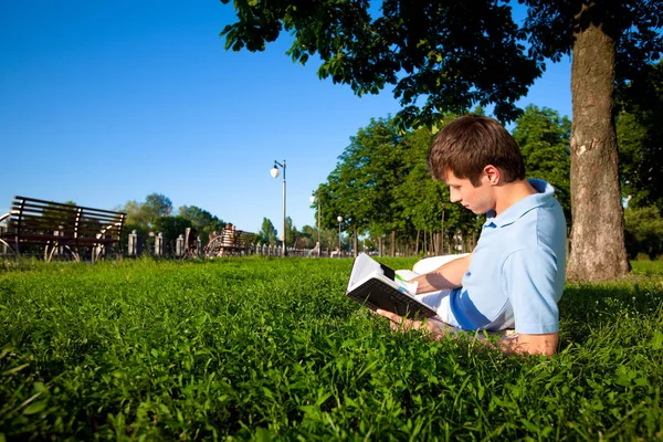 Joven acostado sobre hierba verde en los árboles y leyendo el libro —  Fotos de Stock