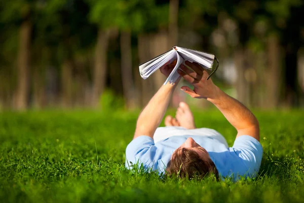 Młody człowiek leży na zielonej trawie i czyta książki — Zdjęcie stockowe