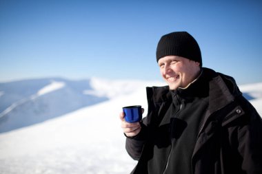 Kış giysileri içinde gülümseyen genç adam termostan çay içiyor.