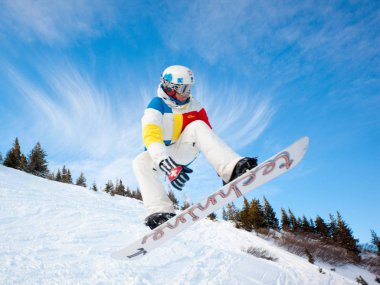 Kış boyunca tepelerde snowboard yaparken atlayan spor giysili genç adam.