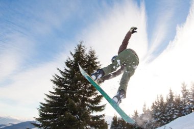 Kış boyunca tepelerde snowboard yaparken atlayan spor giysili genç adam.