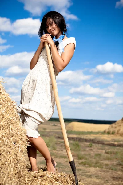 Jeune femme en robe blanche debout avec fourche à foin dans la main dans le champ — Photo