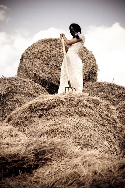 Jeune femme en robe blanche debout avec fourche à foin dans la main dans le champ — Photo