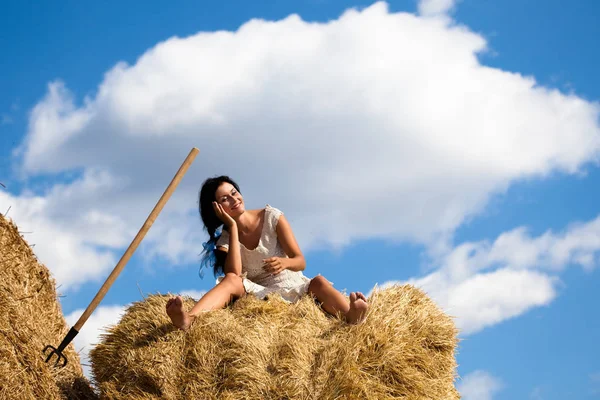 Jeune femme souriante en robe blanche assise sur une pile de foin — Photo