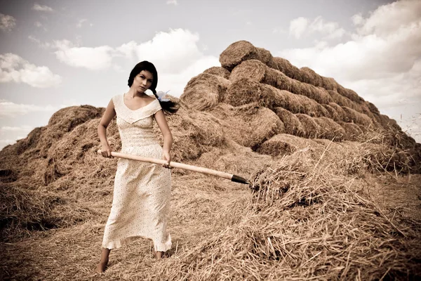 Mujer joven en vestido blanco de pie con horquilla de heno en la mano en el campo — Foto de Stock